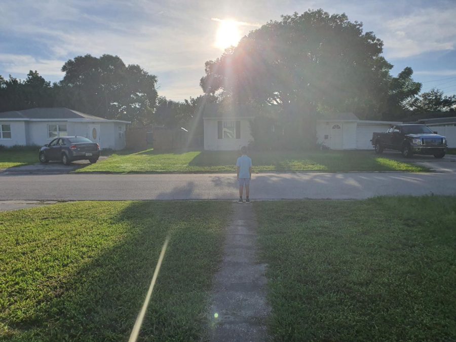 Kid stands in the middle of a side walk which then leads to the subject/kid. Also he is looking at his neighbors house that is across the street.