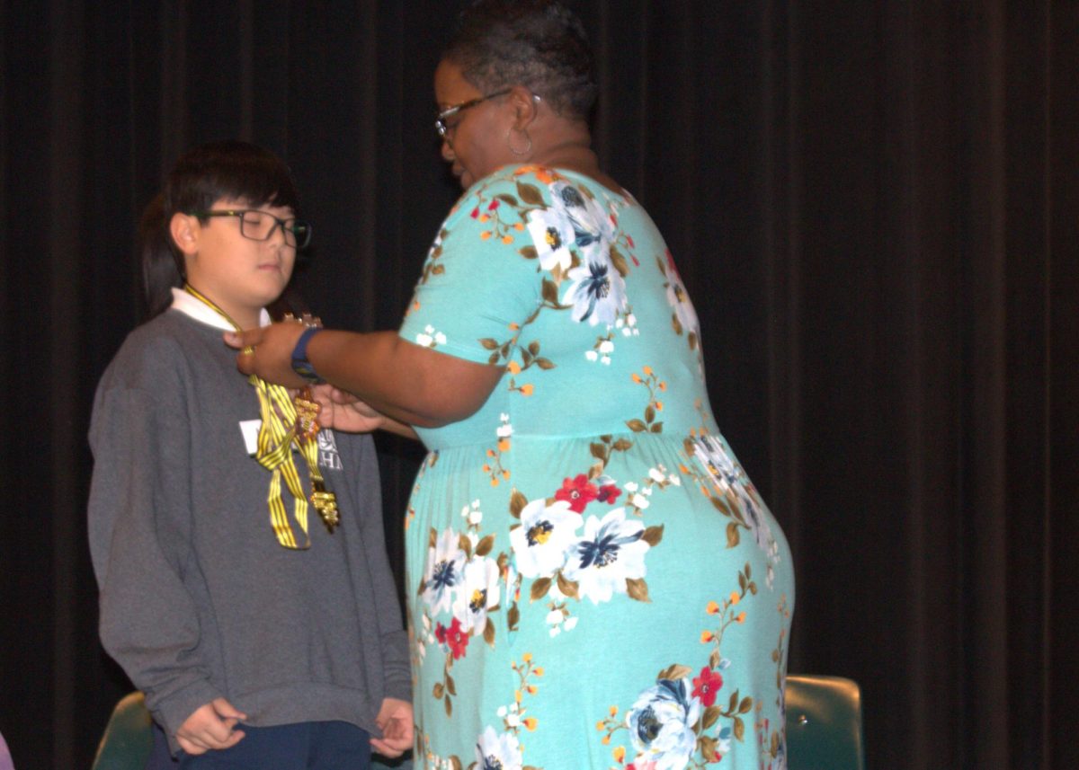 The John Hopkins Spelling Bee Champion Max Mahaz receives his medal from tournament host Ramona Jones.